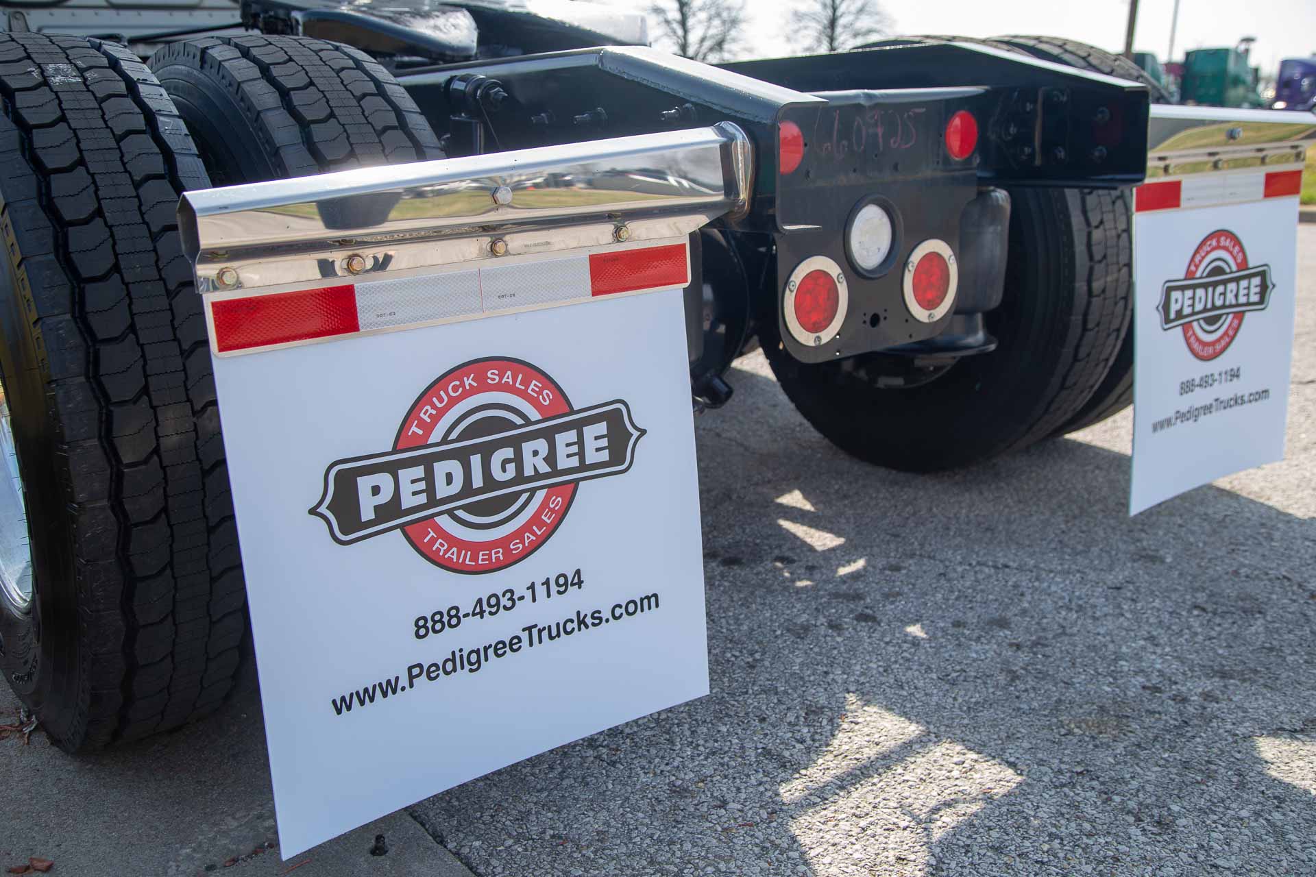 White mud flaps with the Pedigree Truck & Trailer Sales logo attached to the back of a semi-truck.