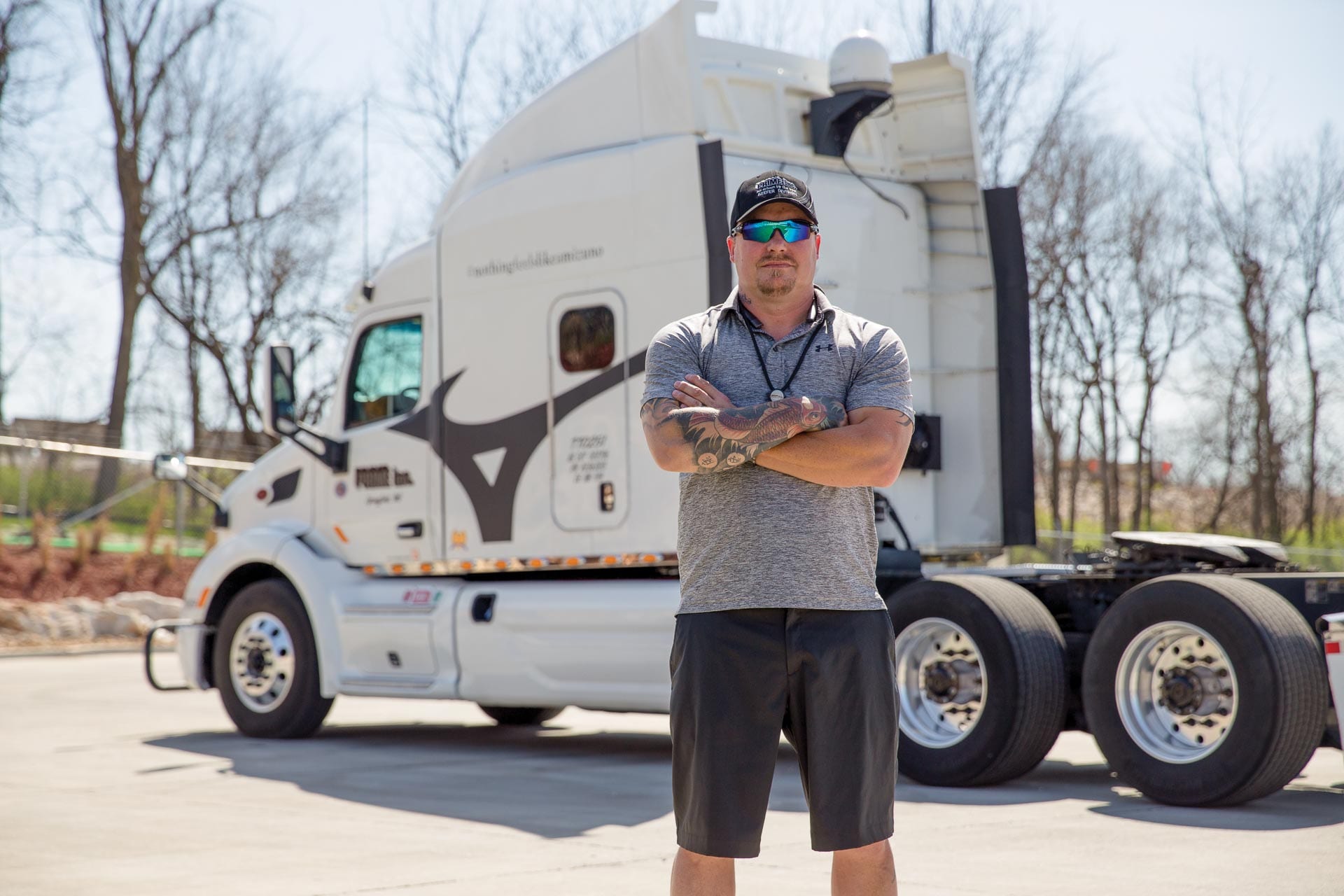 Prime truck driver standing, arms crossed, in front of a white semi-truck with a black Mizuno graphic.