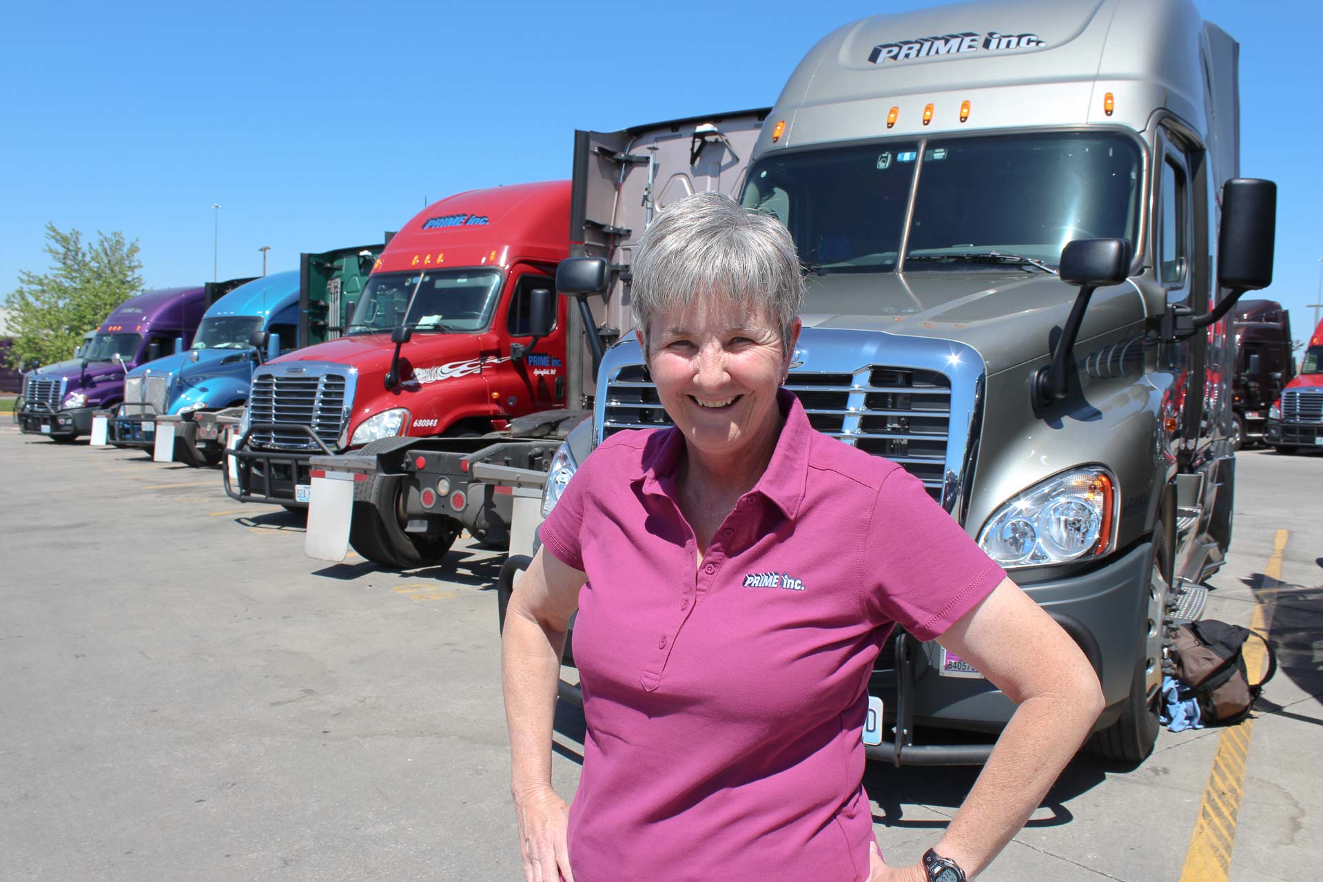 Reba Hoffman, a female truck driver at Prime, standing in front of a row of Freightliner semi-trucks.
