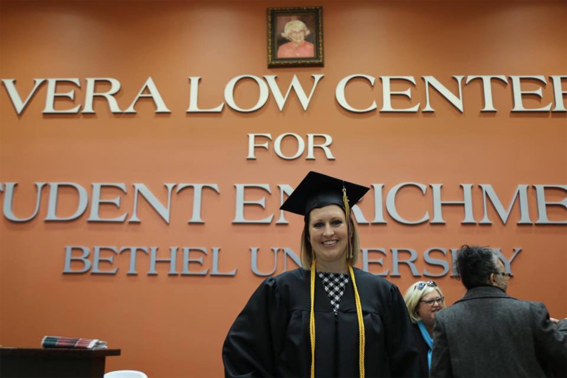 A Prime, Inc. team member, in her graduation gown and hat, standing inside of the Vera Low Center for Student Enrichment.