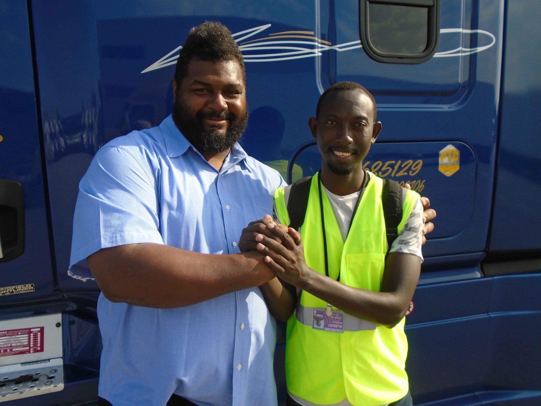 A Prime, Inc. student driver posing for a picture in front of a blue semi-truck with his instructor.