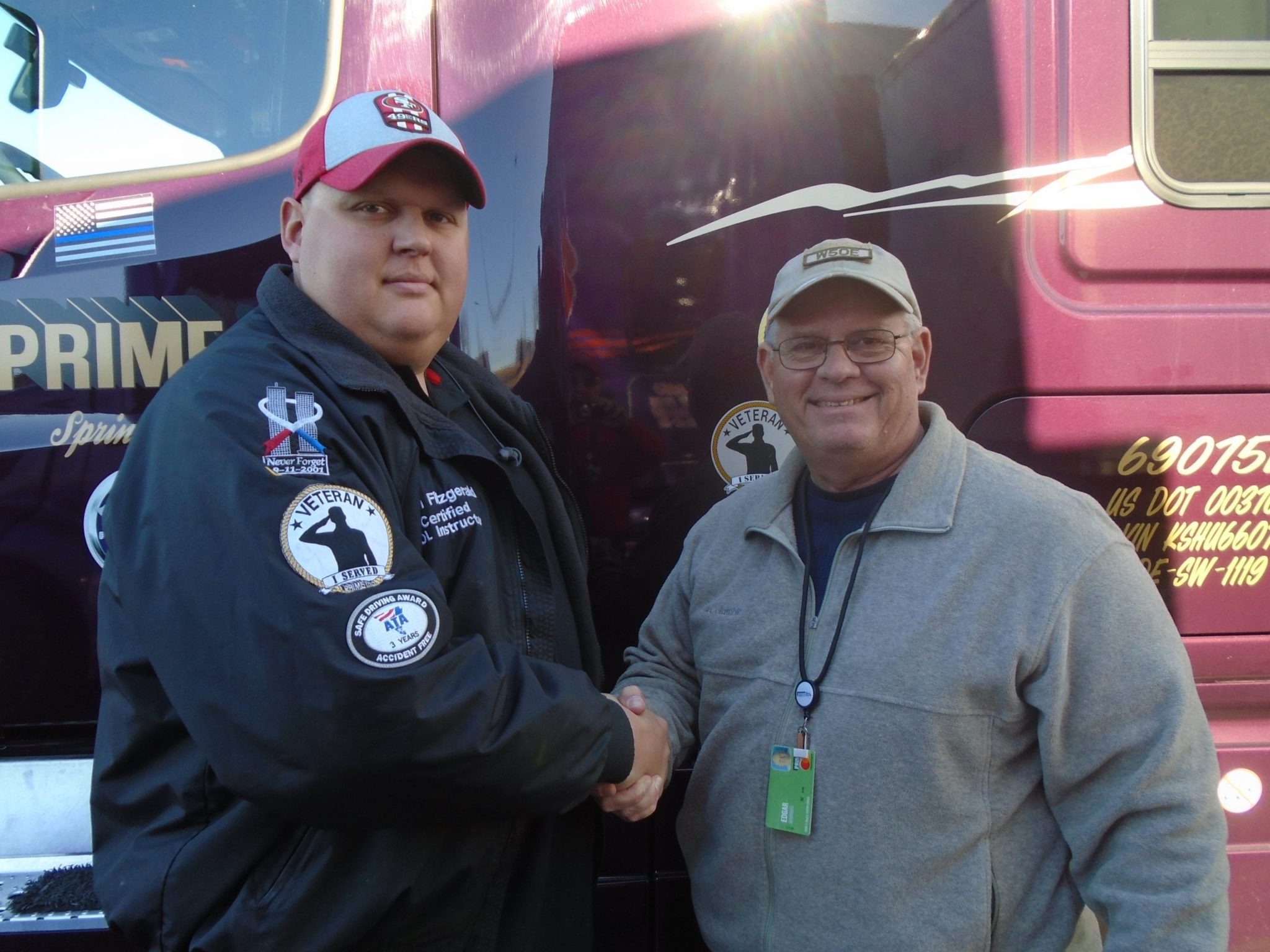 Prime driver and instructor shake hands in front of semi-truck.