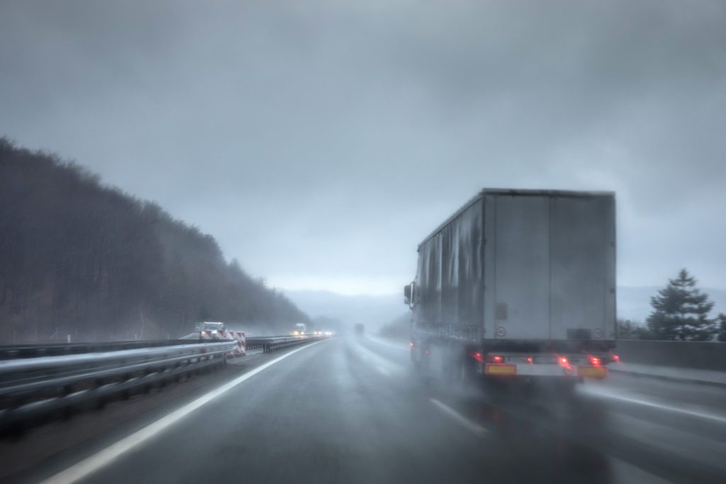 Semi-truck driving in bad weather conditions on rain-soaked road.