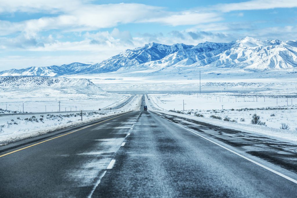 Long perspective of a snowy highway Utah, USA with mountain peaks in the distance.