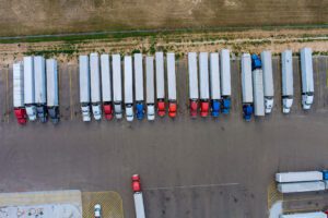 Aerial view of trucks and trailers parked in a line of parking spaces at a rest stop.